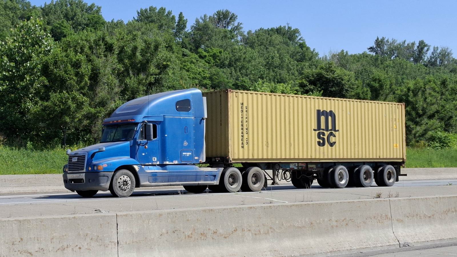 Un camion bleu tirant un conteneur maritime sur une autoroute de Montréal.