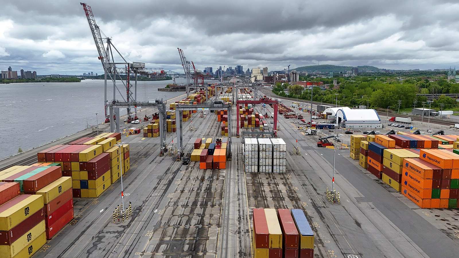 Vue en hauteur des piles de conteneurs et des grues d'un terminal du Port de Montréal, au bord du fleuve Saint-Laurent.